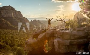 Photo is of a woman standing on a large rock or hill looking out over a valley