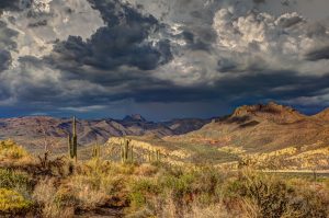 Photo is overlooking a desert valley with mountains in the background and large storm clouds in the sky