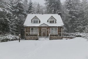 Small cabin in the woods in the wintertime with snow covering the yard and falling